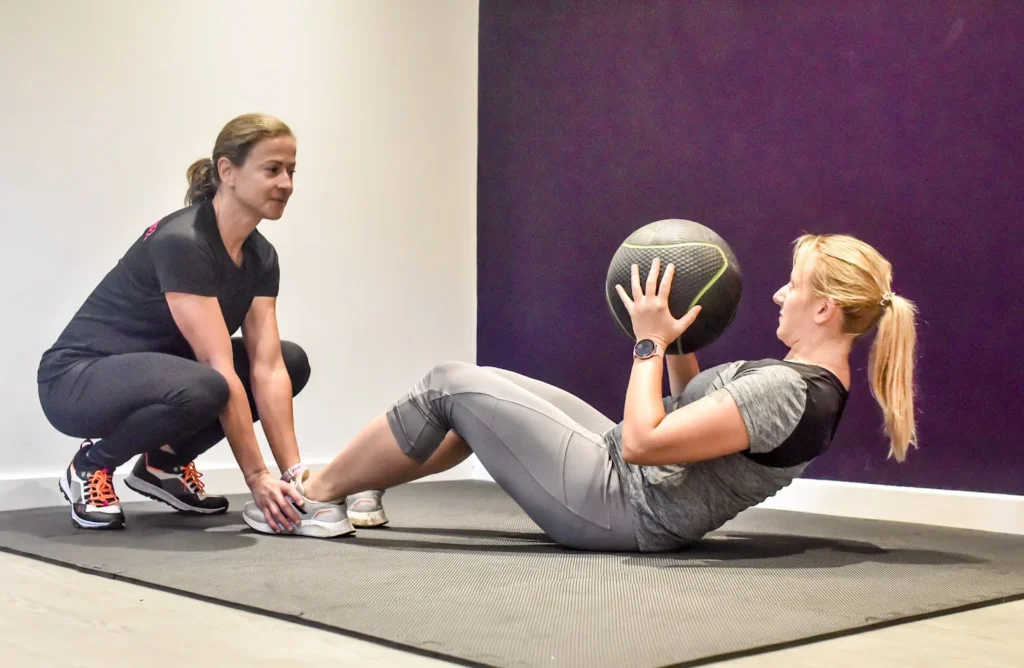 Personal trainer supporting a client doing sit ups with a medicine ball