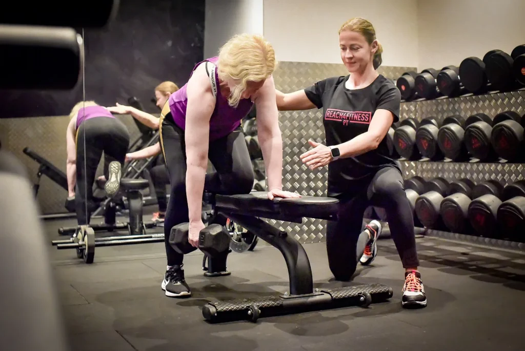 Personal trainer guiding a client's form doing dumbell pulls